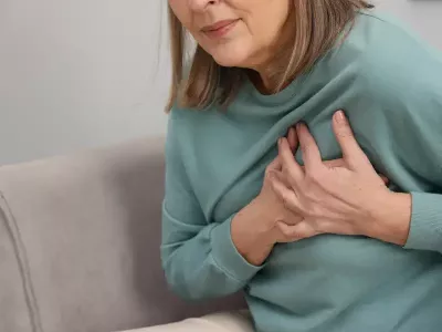 Žena drži ruku na grudima zbog bola u grudima, jednog od prvih simptoma infarkta srca.